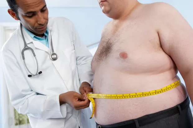 Medico che misura la circonferenza addominale a un paziente obeso con maglia azzurra utilizzando un metro da sarto, per valutare i rischi legati all’obesità.