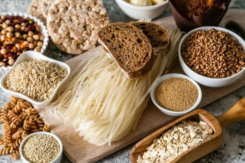 Una tavola imbastita con farine varie, fette di pane di segale e cereali, alimenti privi di glutine consigliati per chi ha allergia o intolleranza al glutine.