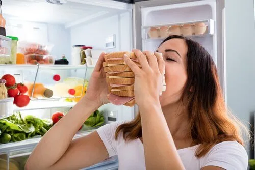 Una donna davanti al frigo aperto che addenta un gigantesco panino come effetto della fame di rimbalzo dovuto alla terapia con Mounjaro.