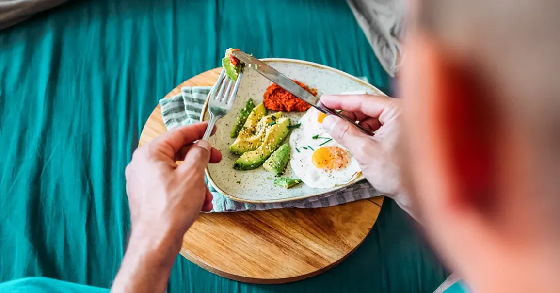 Un uomo di spalle con davanti un piatto con avocado e uova per integrare grassi buoni durante il percorso farmacologico dimagrante.