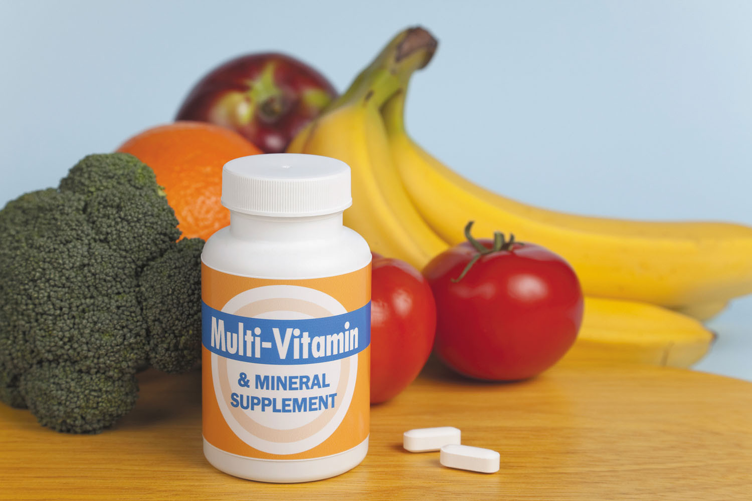 Una confezione di vitamine e minarli in compresse con sullo sfondo frutta e verdura ad indicare l'importanza di questi micronutrienti durante un percorso farmacologico dimagranti.