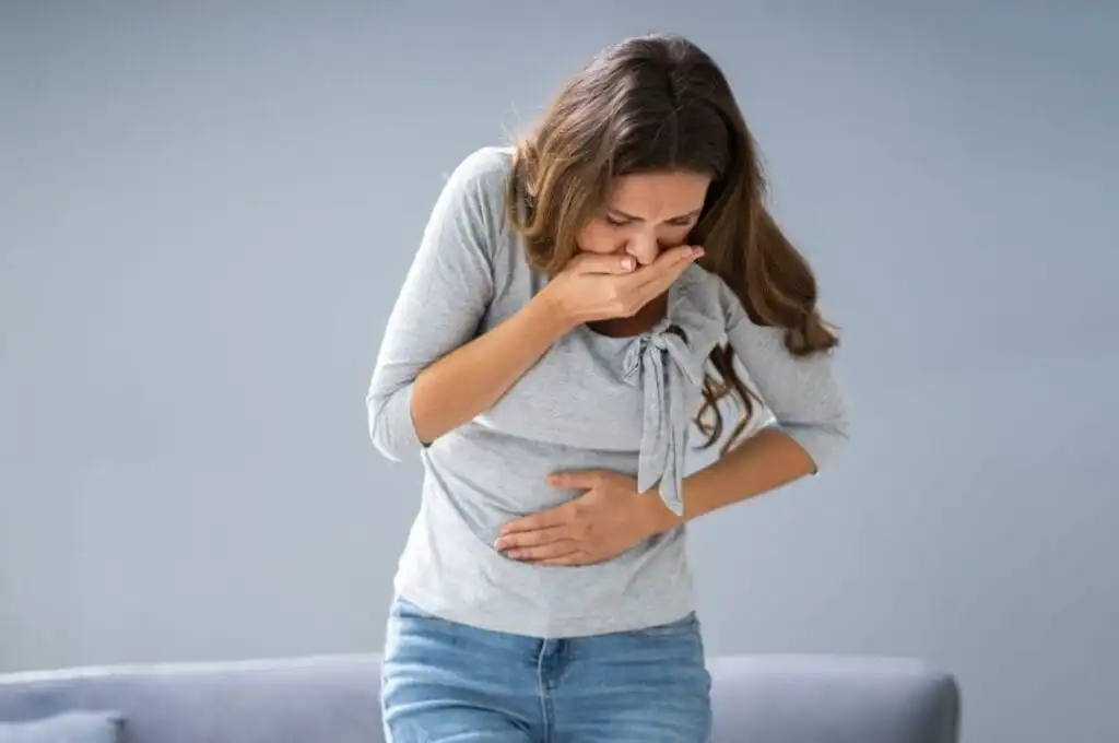 Una donna che si tiene la pancia e copra la bocca che soffre per la nausea da mounjaro.