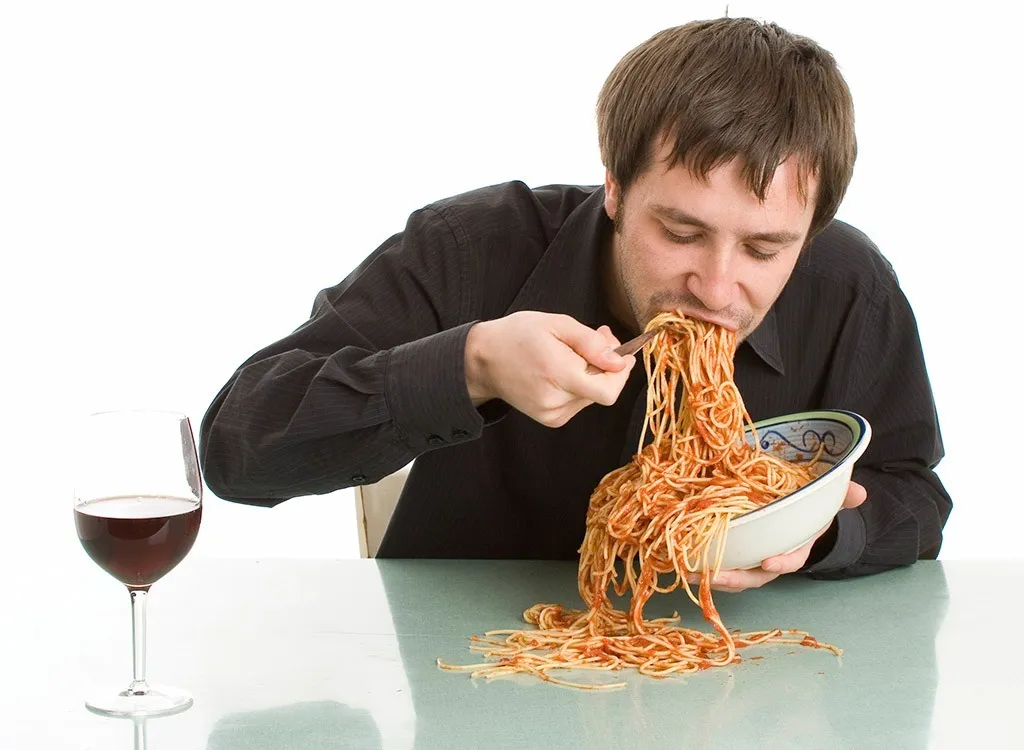 uomo che si abbuffa di spaghetti e vino ad indicare l'errore dei abbuffarsi durante una terapia con mounjaro.