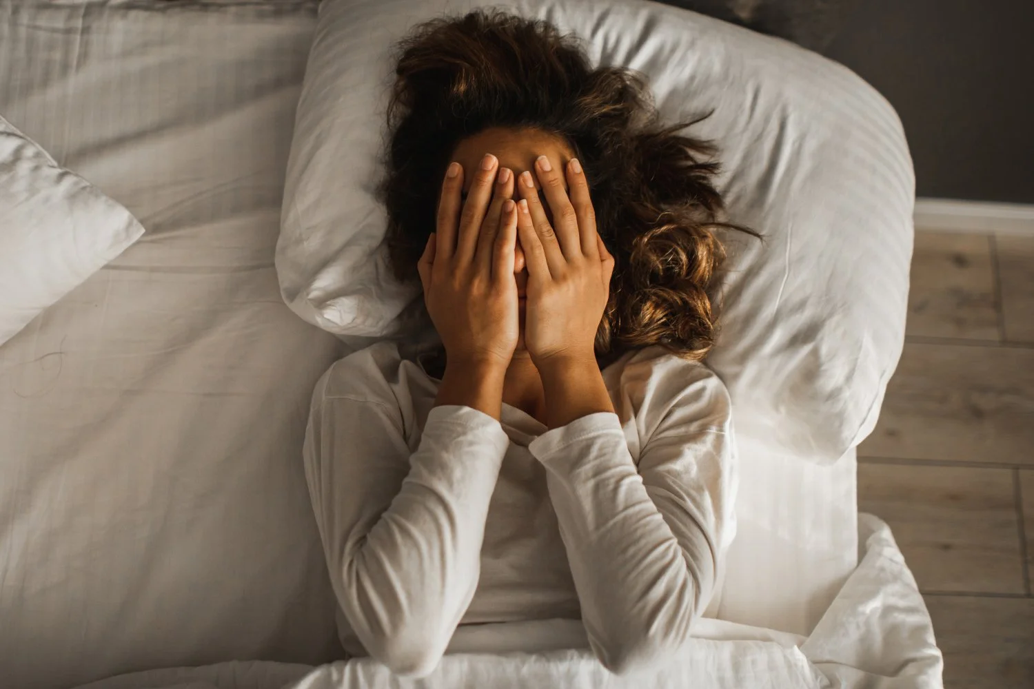 una donna con problemi di sonno durante la terapia con mounjaro, stesa a letto e con le mani sul viso.